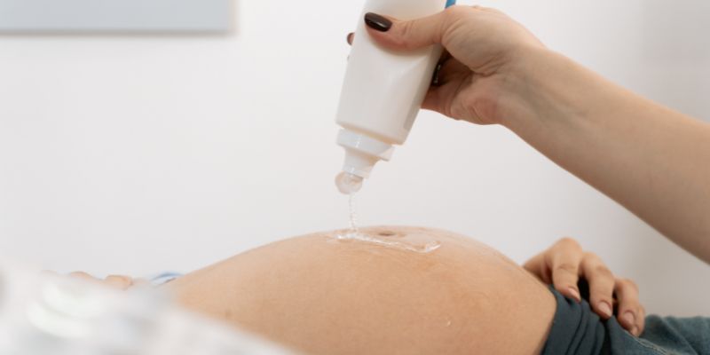 Woman putting ultrasound gel on pregnant woman's belly.