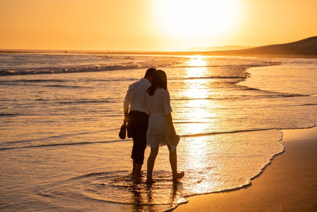 couple holding hands romantically while walking down the beach at sunset