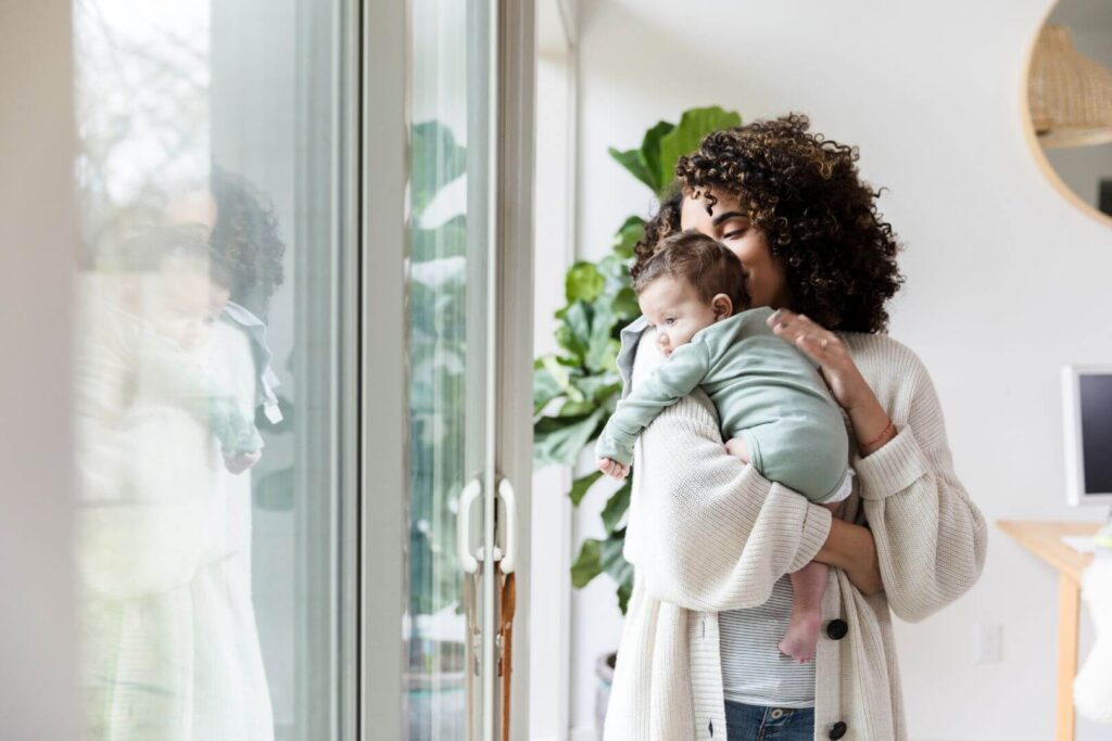 happy single mom with baby in arms looking out the window