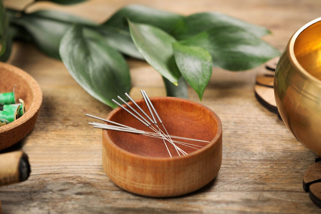 Zen image of acupuncture needles in wooden bowls and leaves in the background