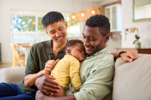 interracial gay couple holding baby on couch