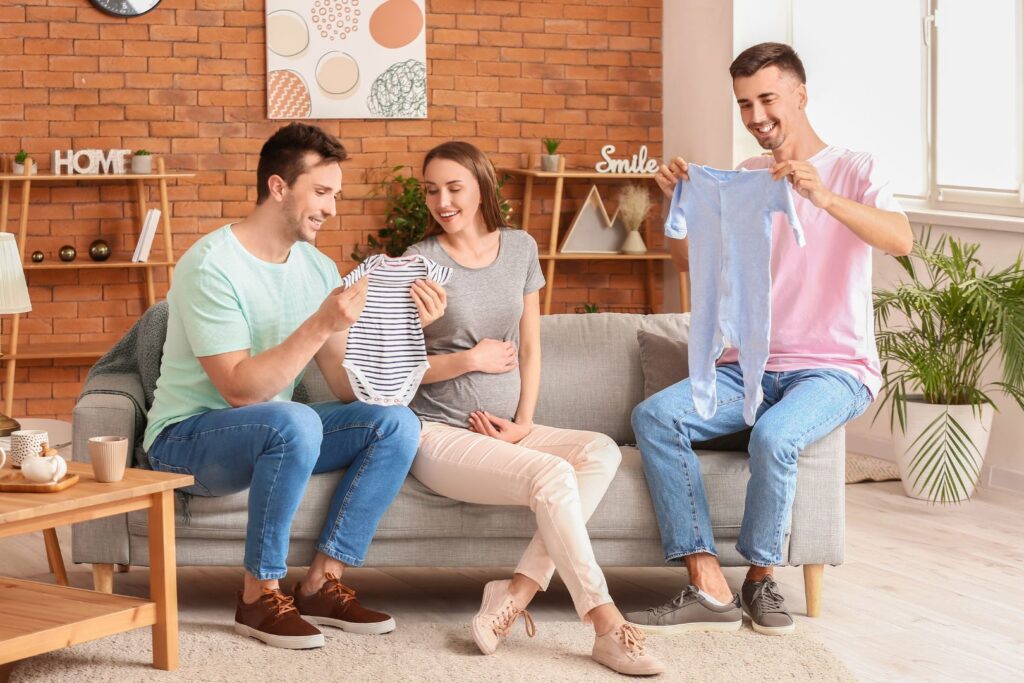 Two intended dads with surrogate sitting on couch looking at baby clothes
